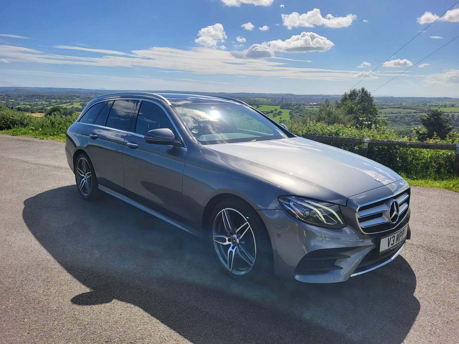 The Top Marks Airport Services Mercedes-Benz E-Class Estate parked on a lane above open countryside